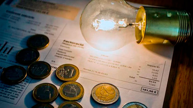 Imagen de una factura de la luz, con una bombilla encendida y varias monedas de euro.